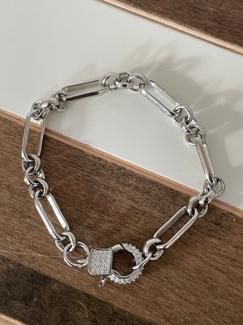 May include: A silver chain bracelet with a silver clasp that is encrusted with small clear stones.