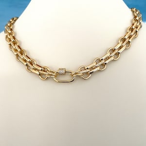 May include: A gold chain necklace with a double chain design and a small, diamond-encrusted clasp.