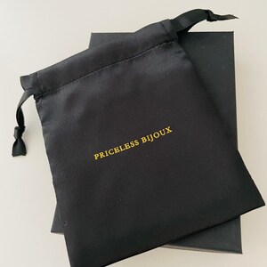 May include: A black satin drawstring bag with the text "PRICELESS BIJOUX" printed in gold.