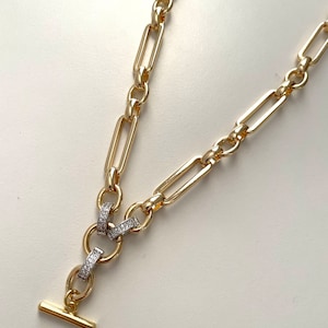 May include: A gold chain necklace with a T-bar clasp and a decorative link featuring small clear stones.