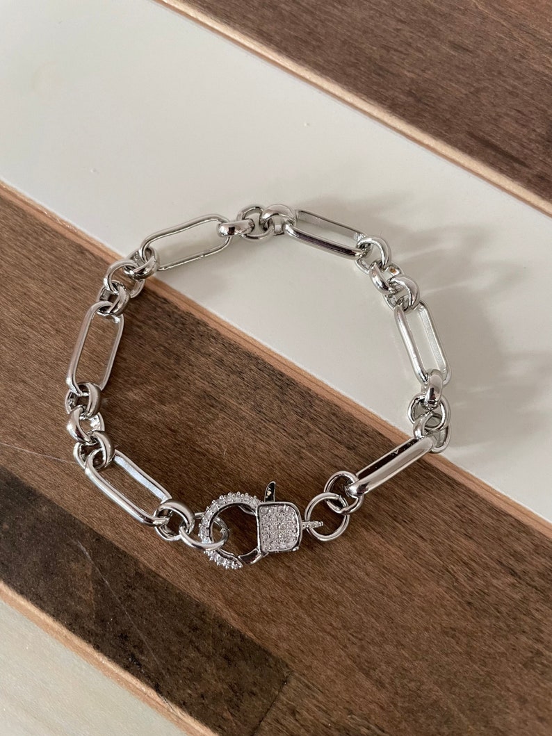 May include: A silver chain bracelet with a silver clasp that is encrusted with small clear stones.