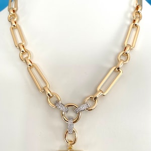 May include: A gold chain necklace with a toggle clasp. The chain is made of large, rectangular links. The toggle clasp is decorated with small, clear stones.