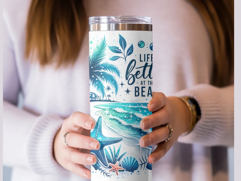 May include: A white stainless steel tumbler with a blue and green beach scene and the text "Life is better at the beach".