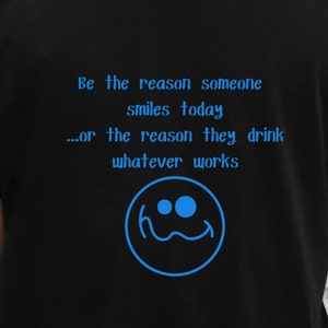 May include: Black t-shirt with a blue graphic that says "Be the reason someone smiles today...or the reason they drink whatever works" and a blue smiley face.