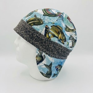Peut inclure: Une casquette en tissu avec un imprimé coloré de divers poissons d'eau douce nageant dans une eau bleue. La casquette présente une large bande texturée gris foncé à la base avec des coutures visibles et un rabat descendant sur la nuque.