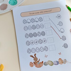 May include: Easter-themed activity sheet with egg patterns and the text "Can you guess what comes next?" A bunny illustration and colorful eggs are at the bottom. Colored pencils and paint palette are in the background.
