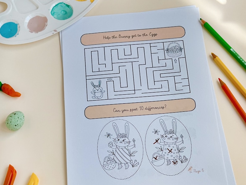 May include: A white paper with a maze and the text "Help the Bunny get to the Eggs". Below the maze is the text "Can you spot 10 differences?". The page also features illustrations of bunnies and Easter eggs. Colored pencils and paint are in the background.