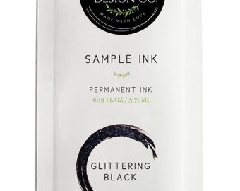 May include: A white sample ink packet with a black circle containing the text "Magnolia Design Co. Made with Love" and the text "Sample Ink, Permanent Ink, 0.19 fl oz / 5.71 ml, Glittering Black".