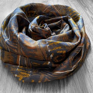 May include: A brown and gold patterned silk scarf with a swirling design. The scarf is rolled up and tied in a knot.