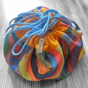 Op de afbeelding: Een kleurrijke trekkoordtas met een gele stoffen voering en een blauw trekkoord. De tas heeft een label met de tekst "ASCALLI" erop.