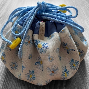 May include: A blue and white drawstring bag with a floral pattern. The bag is made of fabric and has a blue drawstring with yellow toggles.