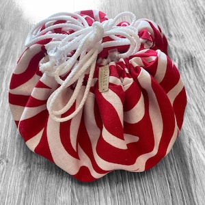 May include: A red and white striped drawstring bag with a white cord. The bag is made of fabric and has a label that says "Sagallit".
