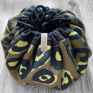 May include: A green and black leopard print makeup bag with a drawstring closure. The bag has a brown leather tag with the text "ASSAULT Linen Products" on it.