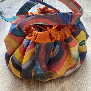 May include: A colourful drawstring bag with a bright orange top and abstract print. The bag has two fabric handles.