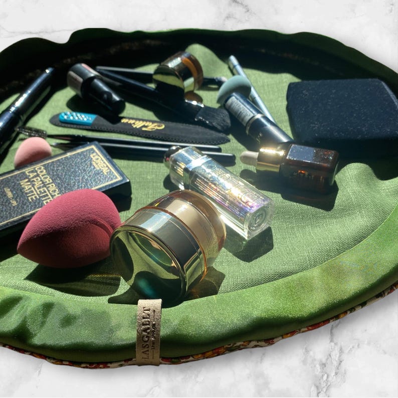 May include: A green makeup bag with a floral pattern and the text "LASSIGALLE" on the bottom. The bag is filled with various makeup products, including brushes, sponges, and containers of cream and liquid.