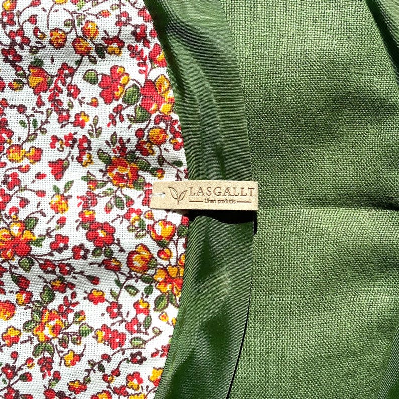 May include: A close-up of a green fabric with a white and red floral pattern. The fabric has a brown leather tag that says "LASGALLT - Linen products".