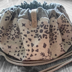 May include: A beige drawstring bag with a black and white geometric pattern. The bag has a brown leather tag with the text "Y LAS GAFAS" on it.