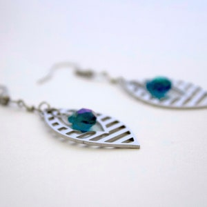 May include: A pair of silver earrings with a leaf design and a blue iridescent gemstone hanging from each earring.