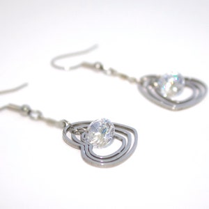 May include: A pair of silver earrings with a clear crystal in the centre of each earring. The earrings are shaped like three interlocking hearts.