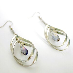 May include: Silver dangle earrings with a teardrop-shaped iridescent crystal hanging from each earring.