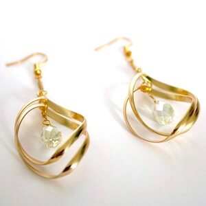 May include: Gold earrings with a delicate, twisted design and a clear crystal dangling from the bottom.