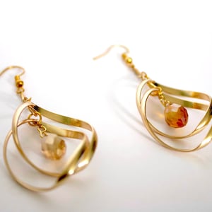May include: Gold dangle earrings with a teardrop shape and a small, clear crystal bead hanging from the bottom.