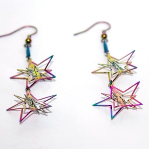 May include: A pair of iridescent rainbow star-shaped dangle earrings. Each earring features two layered stars with a gold bead at the top.