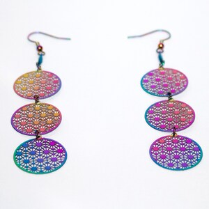 May include: Two pairs of iridescent earrings in a range of colours. Each earring has three oval, openwork pendants with a geometric floral design. The earrings have a hook closure and display a spectrum of colours.