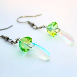 May include: A pair of silver earrings with green and iridescent glass mushroom charms. The charms are shaped like a mushroom with a green top and a clear iridescent bottom.