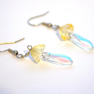 May include: A pair of silver earrings with a yellow mushroom charm and a clear iridescent teardrop dangle.