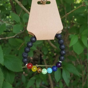 May include: A black lava rock bracelet with seven chakra stones. The stones are red, orange, yellow, green, blue, indigo, and violet.