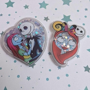Puede incluir: Dos colgantes acrílicos transparentes llenos de purpurina, con personajes de Pesadilla antes de Navidad. Uno tiene forma de corazón con Jack y Sally, el otro es la cara de Sally con un lazo. Los colgantes tienen un borde transparente.