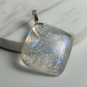 May include: A square glass pendant with a silver bail. The glass is clear with a white and blue iridescent pattern.