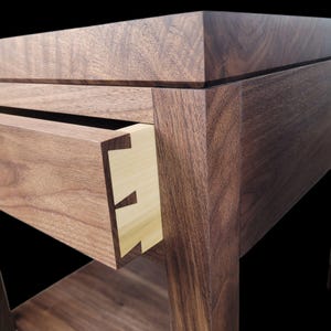 May include: A wooden end table with a drawer and a lower shelf. The drawer is made of light wood and has a dovetail joint. The table is made of dark wood and has a smooth finish.