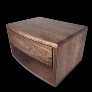 May include: A dark brown wooden bedside table with a curved front and a single drawer. The bedside table has a shelf below the drawer.