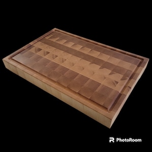 Peut inclure: Une grande planche à découper rectangulaire en bois avec une finition en bois naturel. La planche est composée de plusieurs morceaux de bois disposés en damier. La planche a un bord surélevé autour du périmètre.