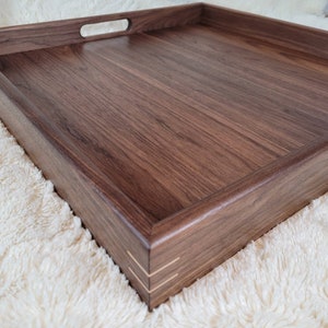 May include: A square wooden serving tray with a dark walnut finish and two handles. The tray has a smooth surface and a raised edge.