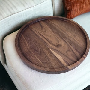 May include: A round wooden serving tray made of walnut wood. The tray has a natural wood finish and a smooth surface.