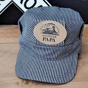 May include: A blue and white striped engineer's cap with a brown leather patch that says "Engineer Papa" and a black and white illustration of a train.