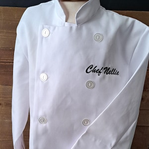 May include: White chef coat with black embroidery that reads "Chef Nellie".