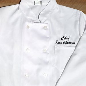 May include: White chef coat with a black embroidered name tag that reads "Chef Rian Christina".