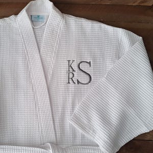 May include: White waffle weave robe with a monogram of the letters "KRS" embroidered on the left chest.