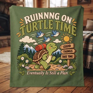 Pode incluir: Uma manta de lã verde sálvia com uma tartaruga de desenho animado com mochila caminhando em um caminho. O texto diz "RUINNNG ON TURTLE TIME" e "Eventually Is Still a Plan" com uma placa "GOOD THINGS TAKE TIME" perto de montanhas, árvores e três pássaros azuis.