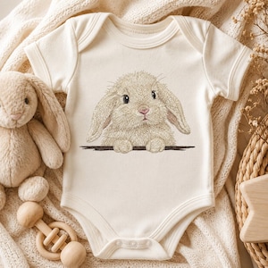 May include: A cream-coloured short-sleeve baby bodysuit featuring an embroidered illustration of a fluffy lop-eared rabbit with long ears, dark eyes, and a pink nose, positioned as if peeking over a dark horizontal line on the chest.