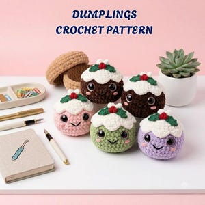 May include: Five round crocheted plushies with white tops, green leaves, and red berries, resembling holiday puddings. They have large black eyes and embroidered smiles. The text DUMPLINGS CROCHET PATTERN appears above. A notebook, pens, and a succulent are nearby.