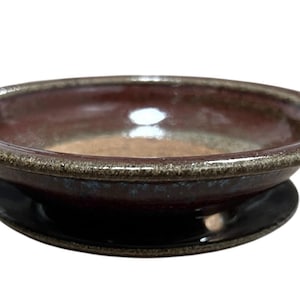 May include: A handmade ceramic bowl with a dark burgundy interior and a dark brown rim. The bowl sits on a black base. The bowl's interior has a glossy finish, and the rim has a textured appearance. This decorative bowl is suitable for serving food.