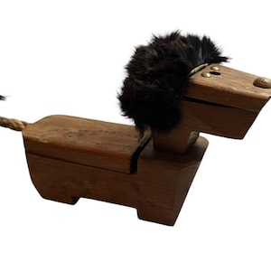 May include: A wooden lion ornament with a dark brown fur mane and tail. The lion has a rectangular body and a head with small brass details. The tail is made of twisted rope. The ornament is a decorative item.