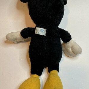 Peut inclure: Peluche d'une c&eacute;l&egrave;bre souris de dessin anim&eacute;, vue de dos. Le jouet est principalement noir avec des gants blancs et des pieds jaunes. Les oreilles sont grandes et arrondies. Une &eacute;tiquette est attach&eacute;e au dos.