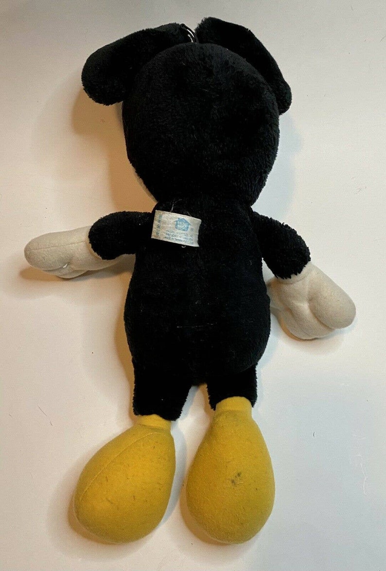 Peut inclure: Peluche d'une c&eacute;l&egrave;bre souris de dessin anim&eacute;, vue de dos. Le jouet est principalement noir avec des gants blancs et des pieds jaunes. Les oreilles sont grandes et arrondies. Une &eacute;tiquette est attach&eacute;e au dos.