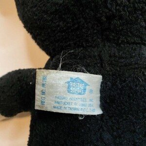 Peut inclure: Gros plan sur un jouet en peluche noir avec une &eacute;tiquette attach&eacute;e. L'&eacute;tiquette indique "HASBRO INDUSTRIES INC PAWTUCKET RI 02862 USA MADE IN TAIWAN R.O.C." Le jouet en peluche a un aspect doux et textur&eacute;.
